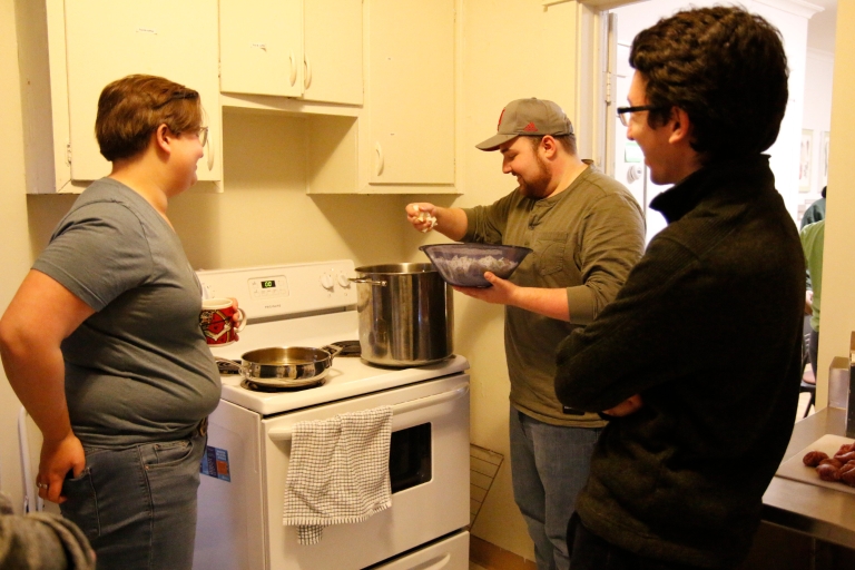 Three students stand around a stove in a kitchen
