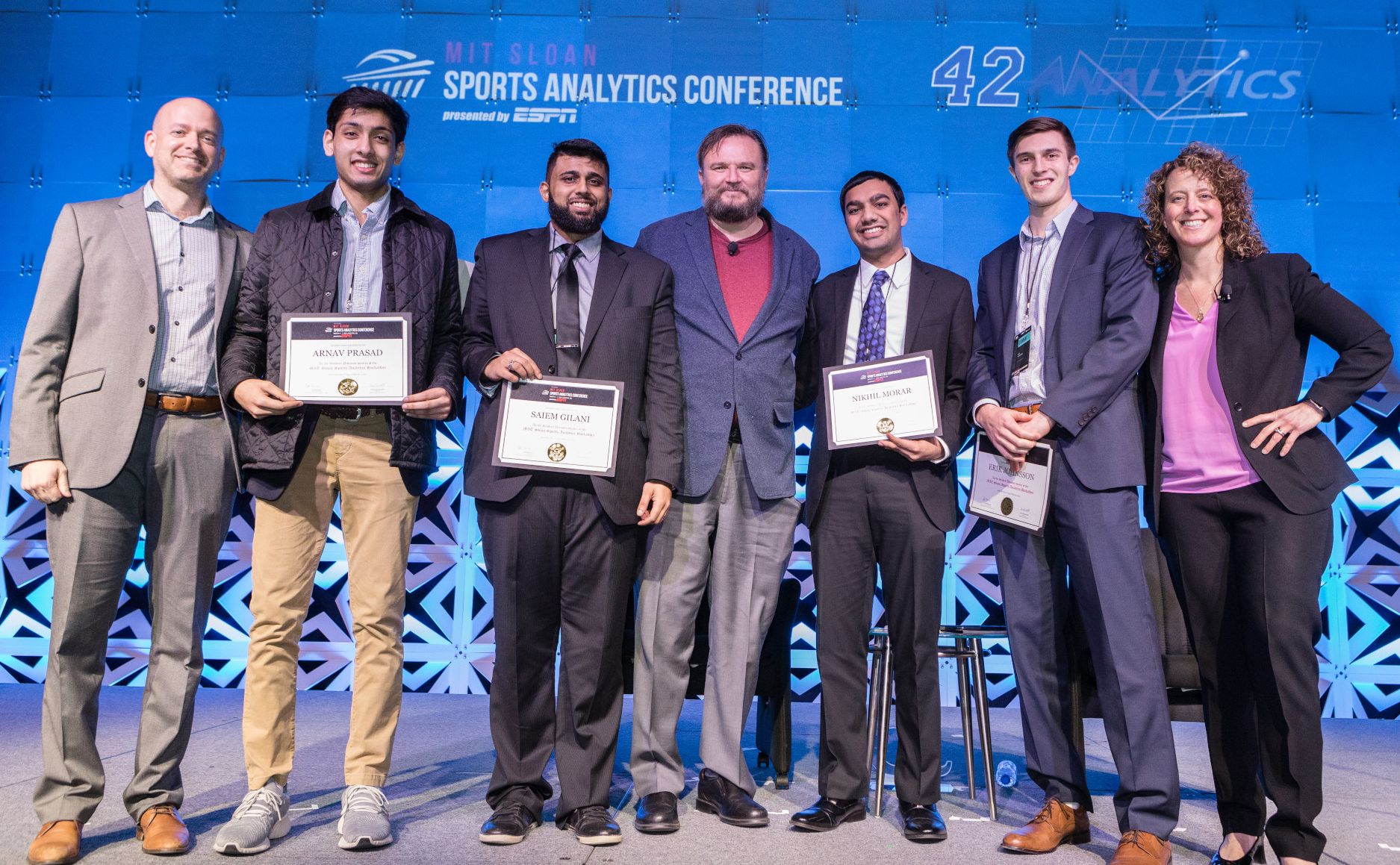 seven people stand on stage at sports analytics conference