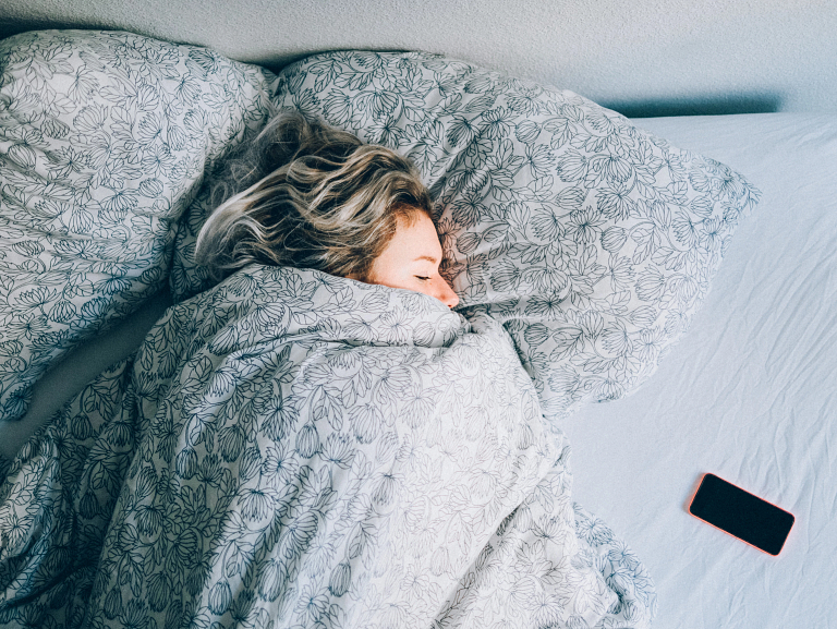 Woman sleeps in bed with covers pulled up over her mouth