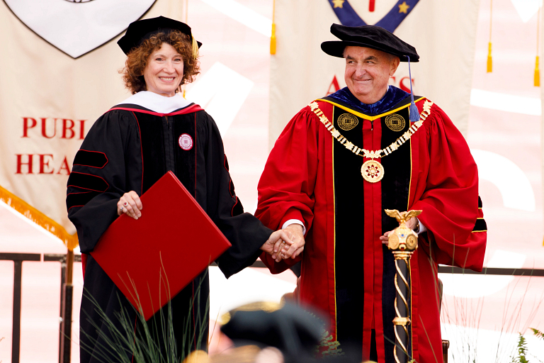 Laurie Burns McRobbie and Michael A. McRobbie stand on stage dressed in graduation robes