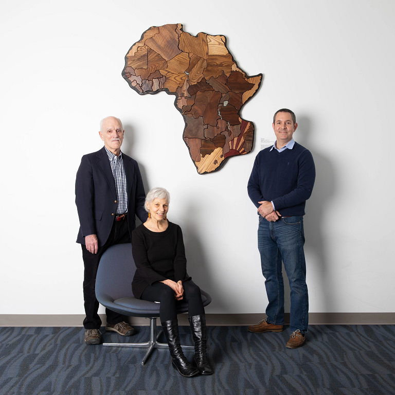 Three people stand beside a large carving of the African continent