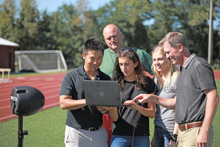 Kei Kawata and colleagues gather on the field to discuss subconcussive impact data