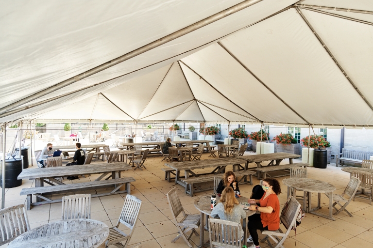 masked students seated at tables under a tent