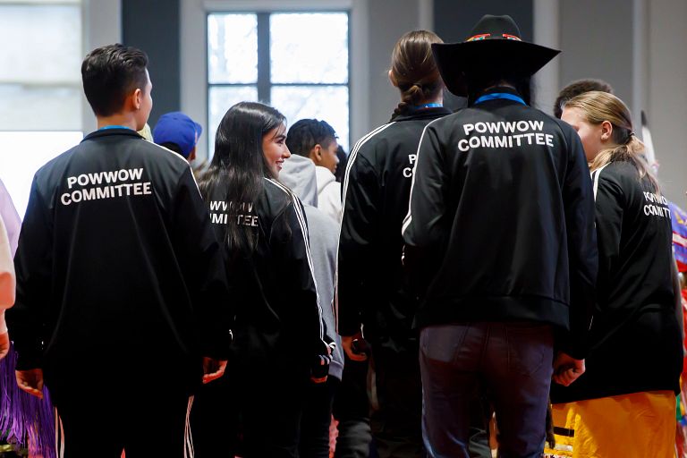 Students stand wearing matching black track suits that read Powwow Committee on the back..