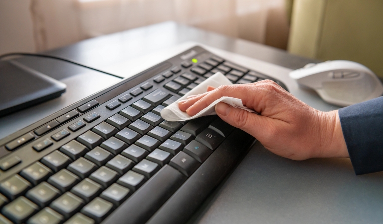 a hand cleaning a computer keyboard with a wipe