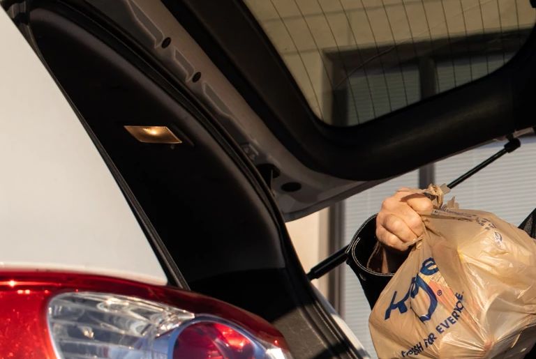 man places packs bags of food in a vehicle for delivery