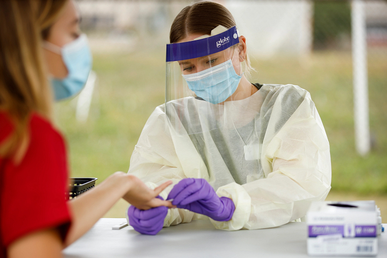 A nursing student collects a blood sample from another IU student under a tent outdoors