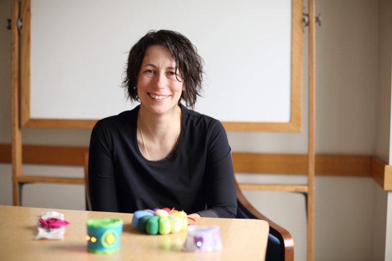 Kylie Peppler smiles at the camera, there is a table with crafts in front of her