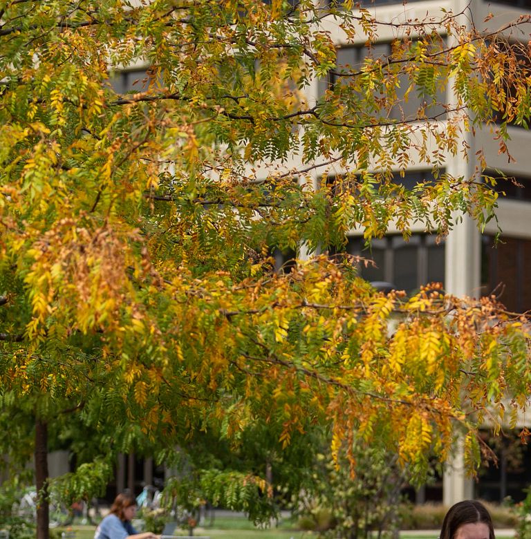 two students wearing masks sitting at a table in front of university library