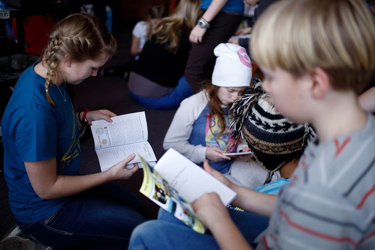 IU student Lillie Hartman sits on the ground and reads the The World Is Our Home, to Harmony School students as part of IU's Books and Beyond. 