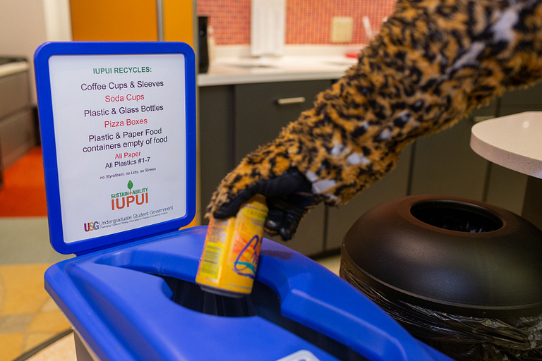 Closeup of the Jaguar mascot's hand putting a drink can in a recycling bin.