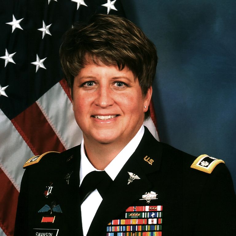A portrait of a woman in front of a flag wearing a military uniform decorated with medals.