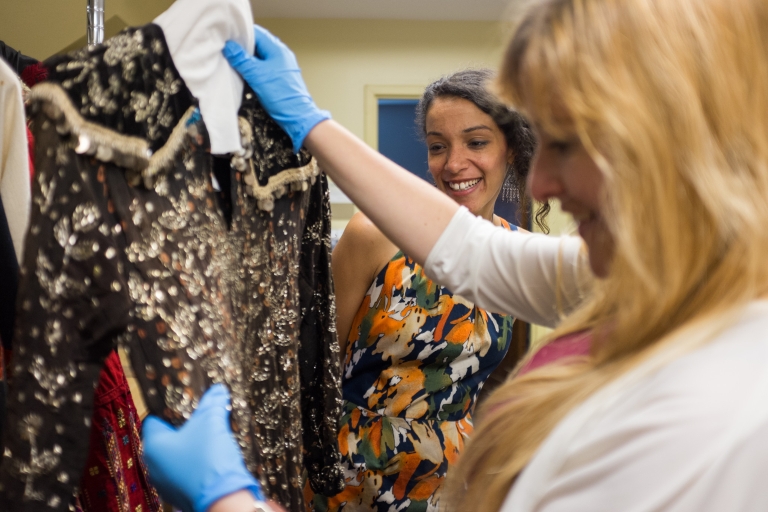 Maggie Slaughter holds a black Syrian wedding dress with gold accents as Kaila Austin watches.