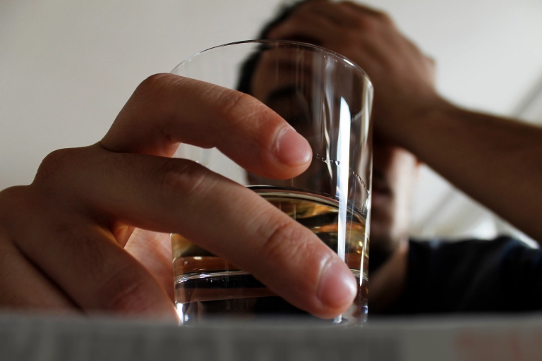 A man holds a glass of alcohol while burying his face in his other hand