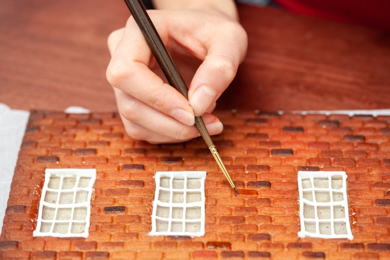 A hand paints pieces of a gingerbread house