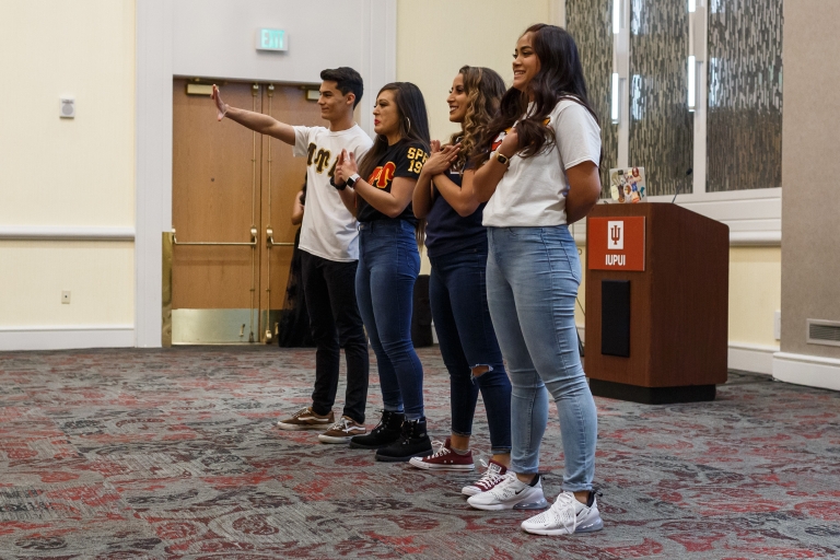 Members of the Multicultural Greek Council stand in a line showing their groups' hand signs.