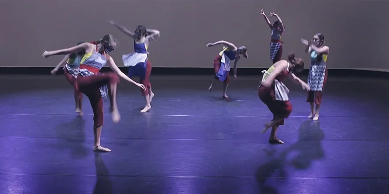 Seven dancers in a circle formation lift legs and arms during performance.