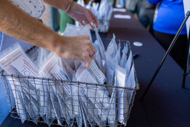 A closeup of hands sorting through a basket of naloxone samples on a table.