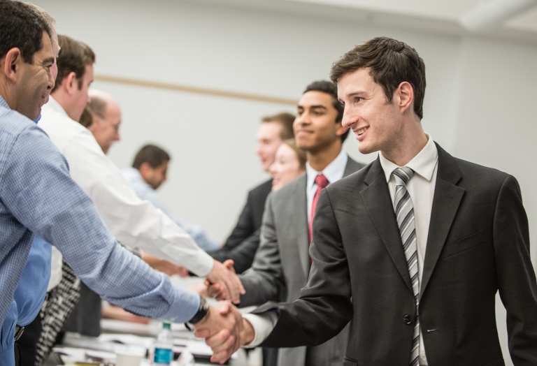 Several students shaking hands with visiting business people