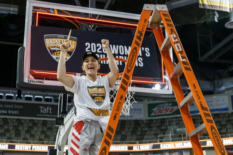 womenâ€™s basketball player stands on a ladder celebrating cutting part of the net