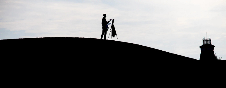 Silhouette of person painting while standing on hill