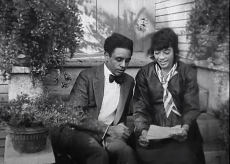 A black and white image of a well-dressed Black man and woman sitting on a stoop together.