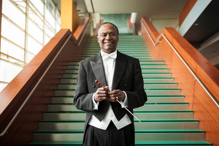 Thomas Wilkins standing at bottom of tall staircase, dressed in tux and holding baton