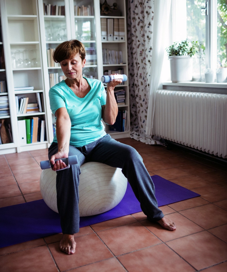 Older woman sitting on an exercise ball performs bicep curls