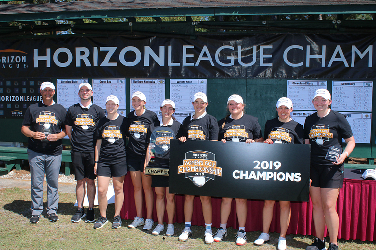Women's golf players hold championship banner.