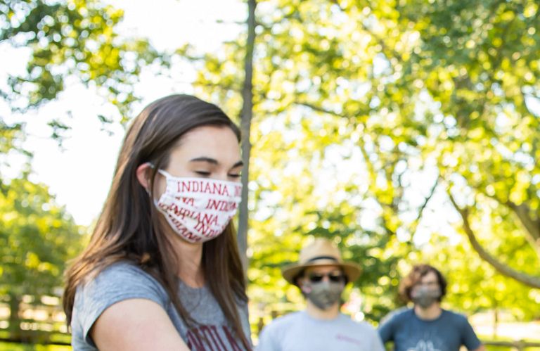 A woman wearing a mask hands a paper to another woman in a mask during an outdoor event