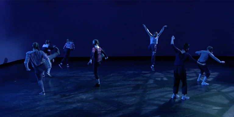 Dancers in blue light face away from one another while posing with extended arms, legs.