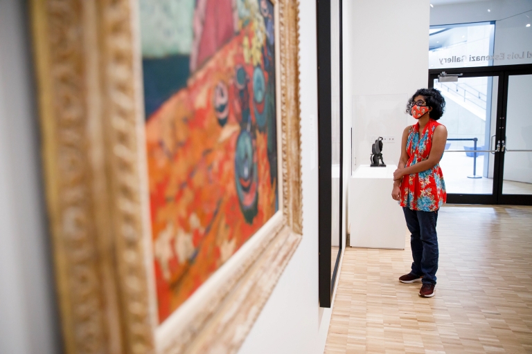 A woman wearing a mask looks at art in a museum