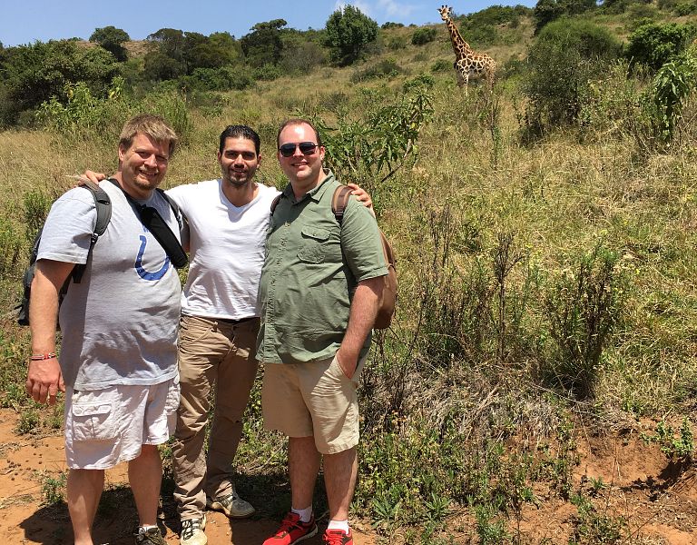 Men stand in front of a giraffe in Kenya.