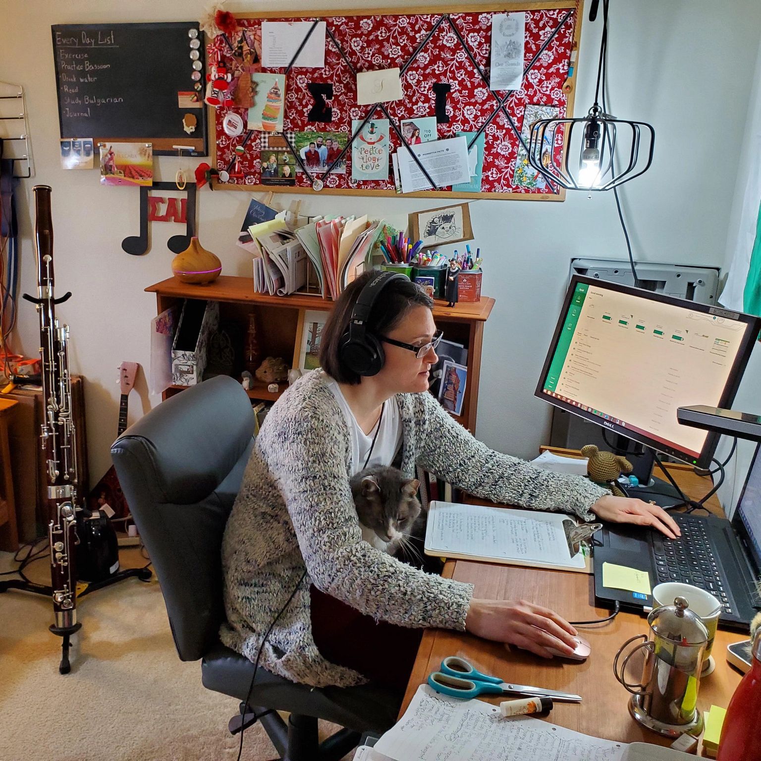 A woman works at her home computer with a cat sitting on her lap.
