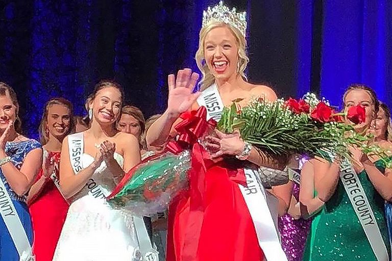 Audrey Campbell waves from a pageant stage in a formal gown and a crown.