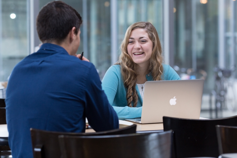 Sarah Grace Fraser speaks with a fellow student at a table.