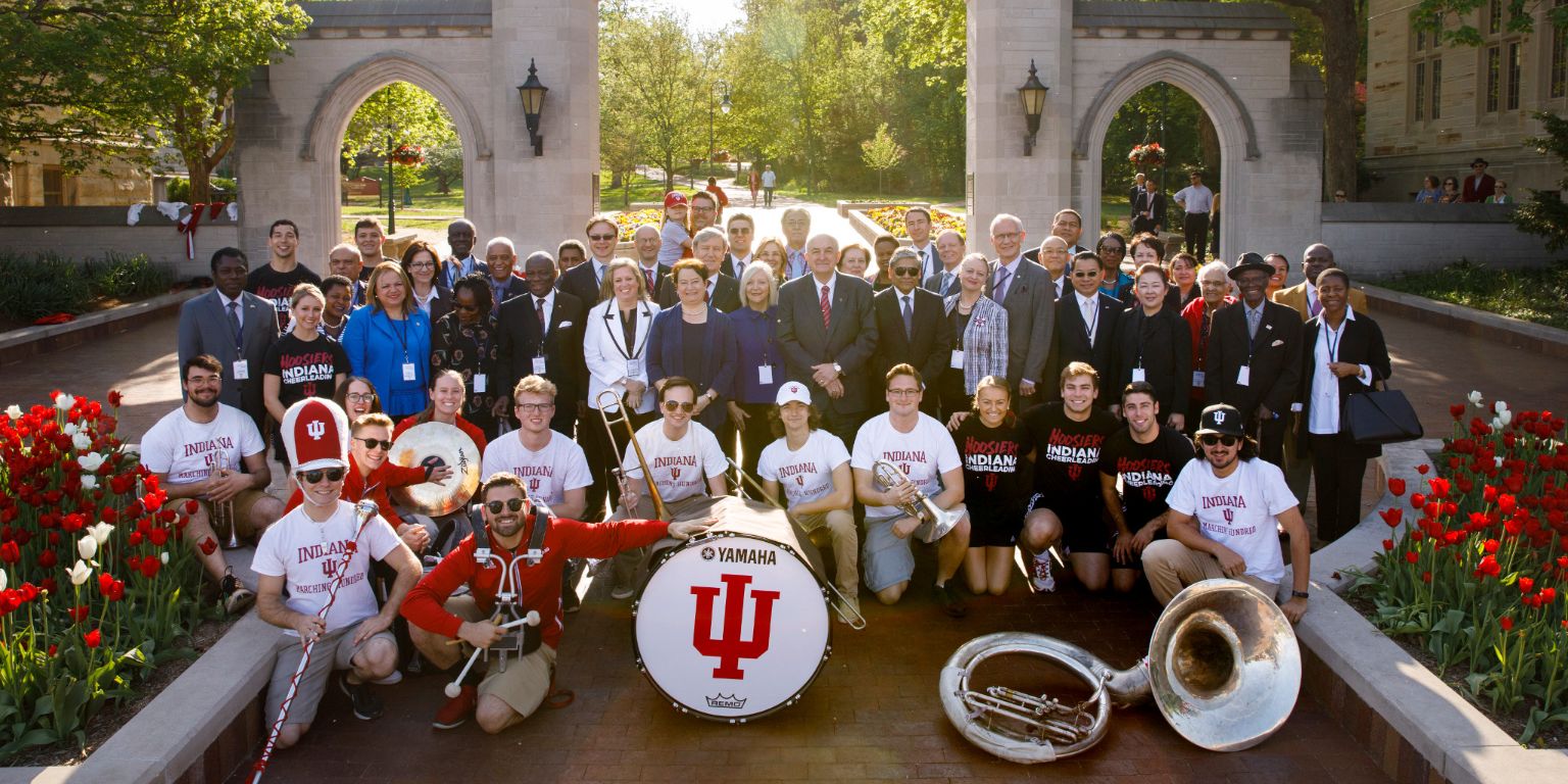 IU leaders and IU Crabb Band members pose with about 30 foreign ambassadors in front of Sample Gates