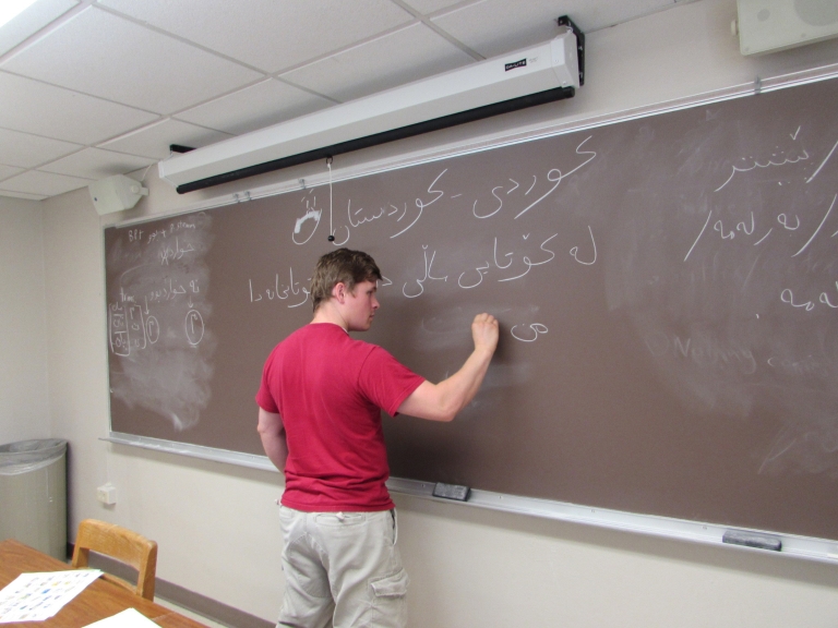 A student writes a foreign language on a chalkboard