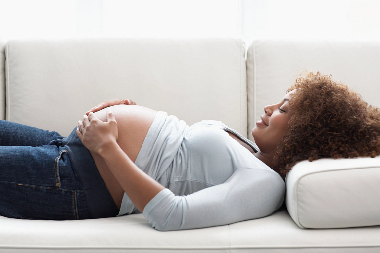 pregnant woman holds belly while lounging on sofa