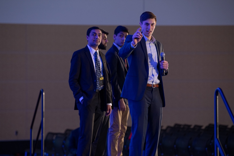 Four men stand onstage, presenting 