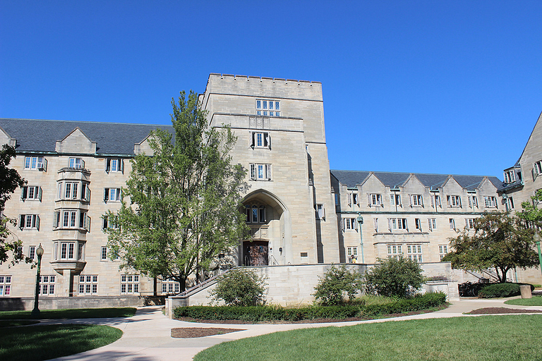 A three-story residence hall made of limestone with trees in front of the building.