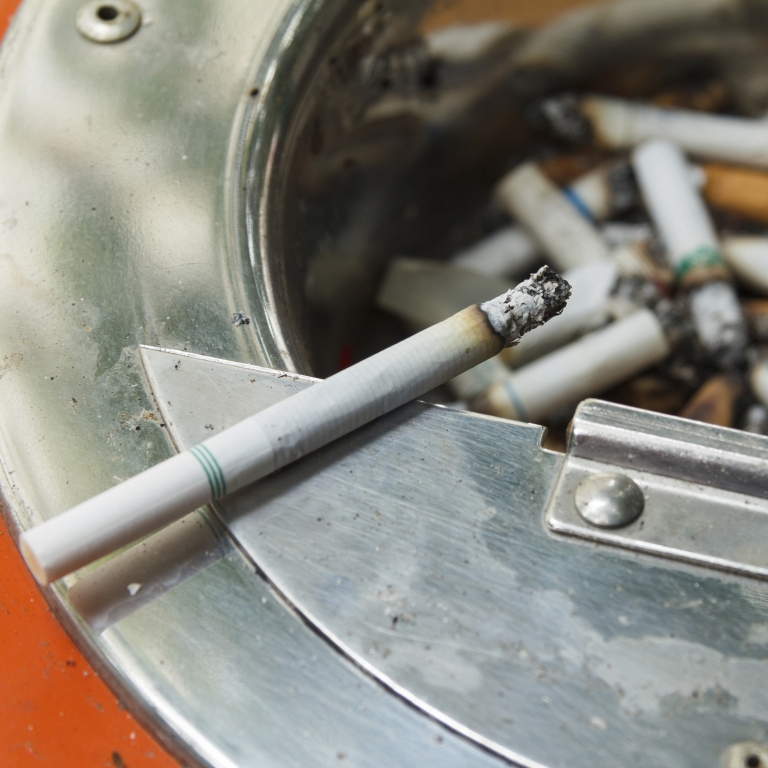 Smoking cigarette sitting in an ashtray.