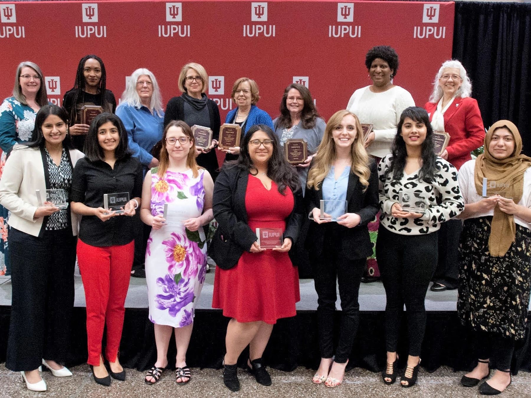 Women stand in front of an IUPUI backdrop holding awards