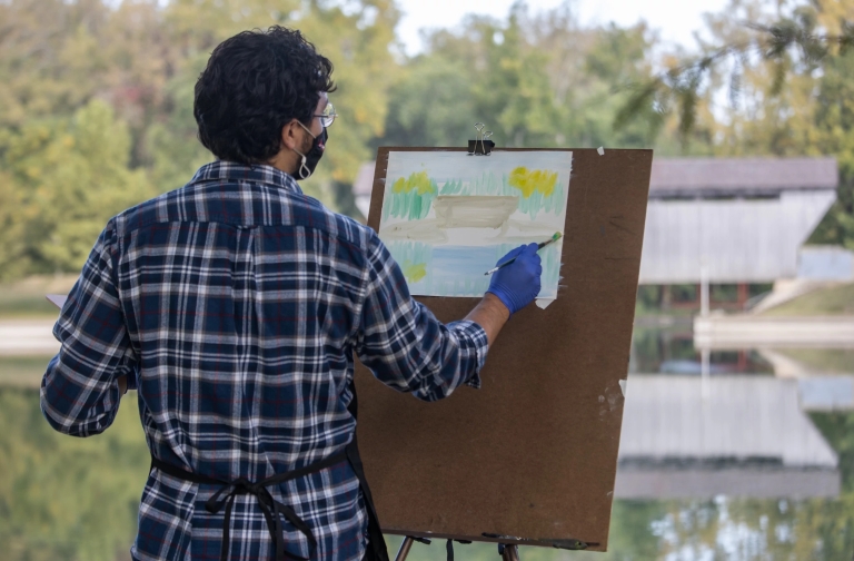 A student paints a covered bridge at Mill Race Park 