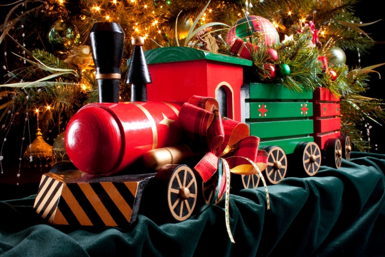 Red-and-green model train decorated for Christmas in front of a tree.