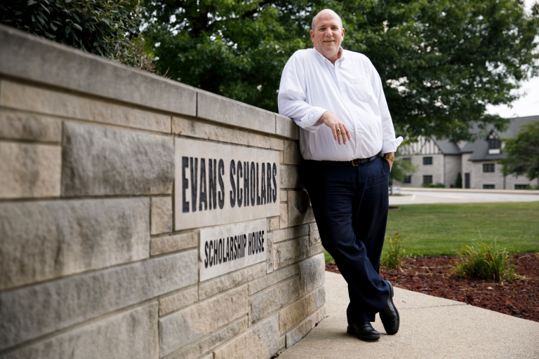 Tom McMahon posing in front of the Evan Scholars sign