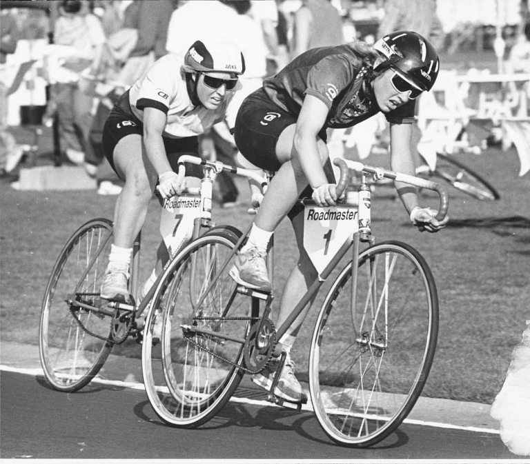 Two women race bicycles on a track.