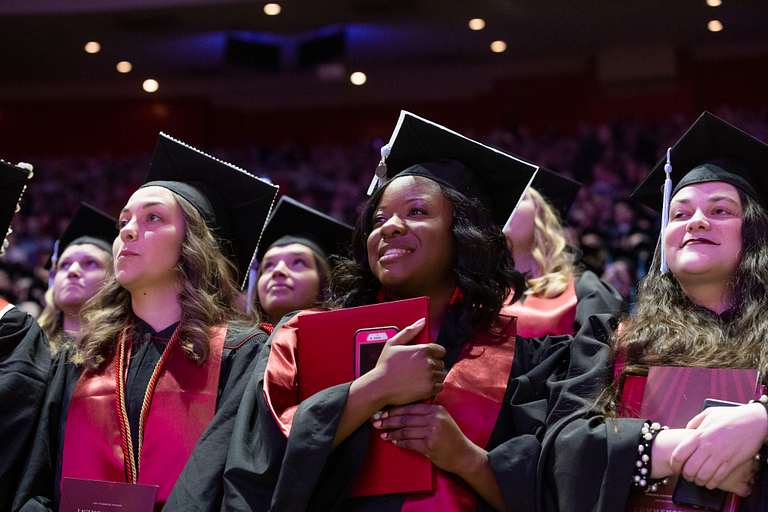 Students wearing caps and gowns hold their degrees during a commencement ceremony