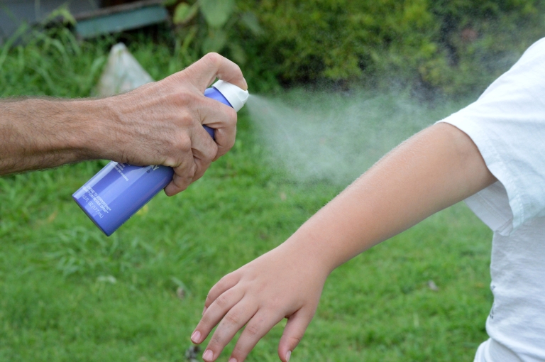 Sunscreen is being sprayed on a child's arm