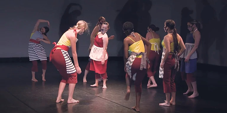 Dancers wearing red and yellow costumes look gravely at the ground.